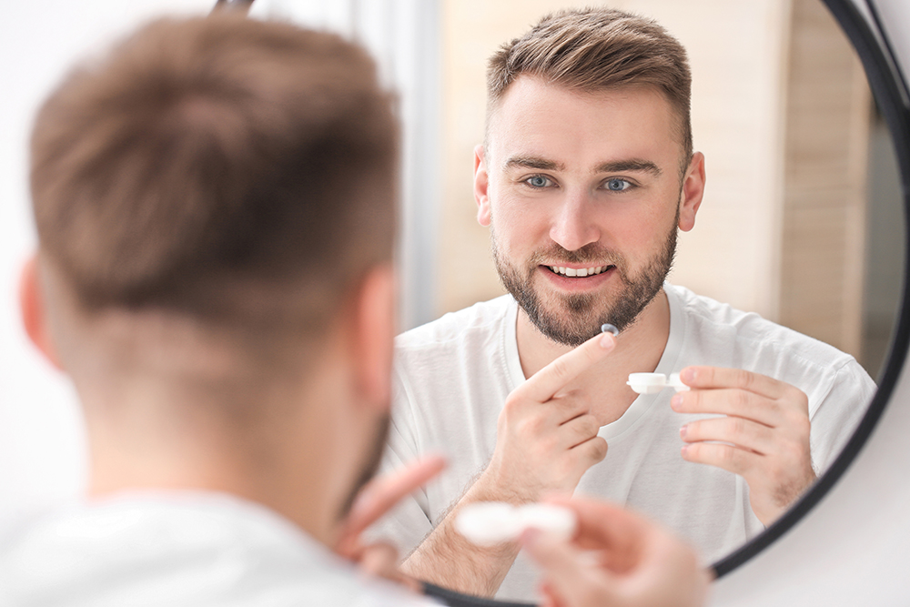 Mann mit kurzen Haaren setzt sich vor Spiegel eine Kontaktlinse sein
