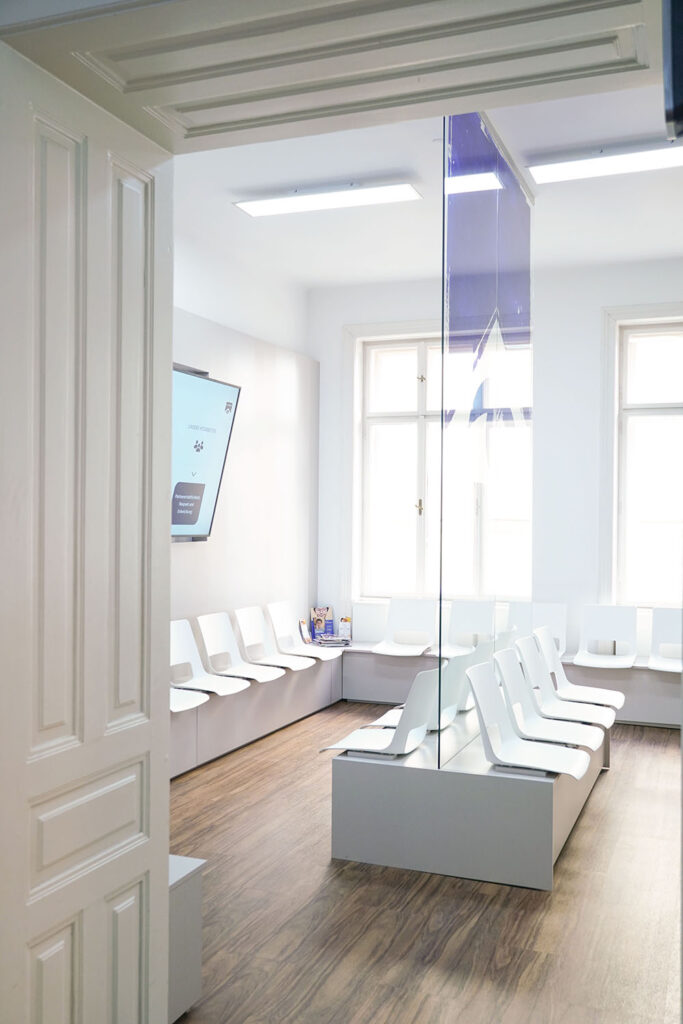 Wartebereich eines modernen Optikstudios mit Sitzplätzen, Bildschirm sowie Glaswand