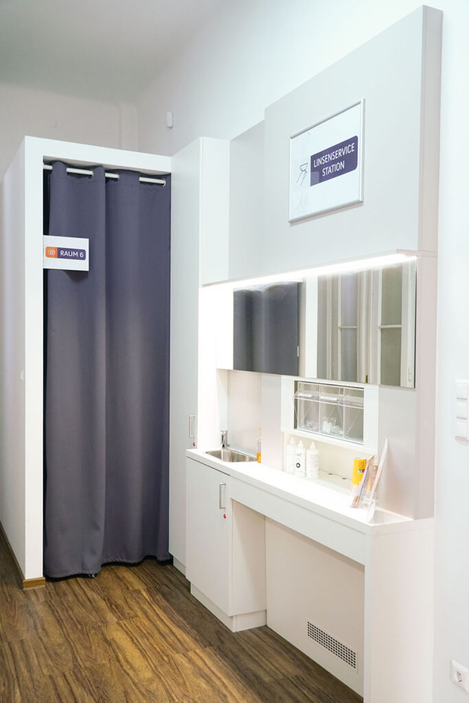Linsenservicestation mit Waschbecken und Spiegel, sowie Vorhang zu anderem Untersuchungsgraum