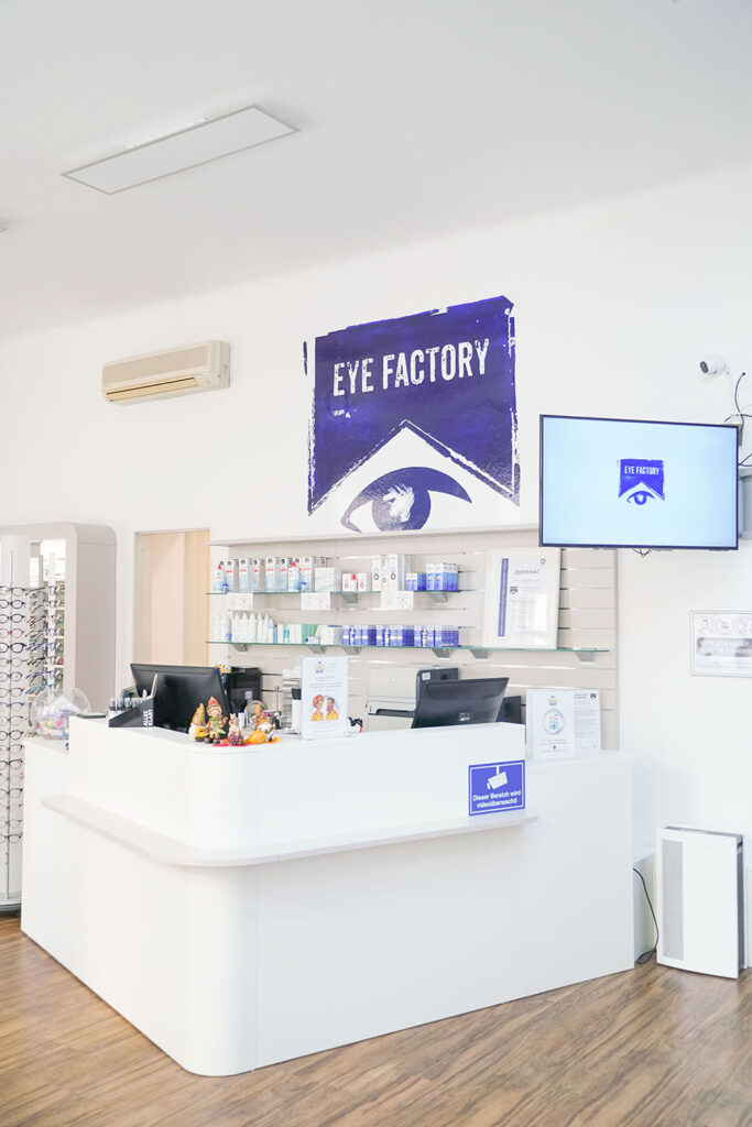 Kassenbereich eines Optikstudios mit Bildschirm an der Seite. Großes Logo an der Wand.