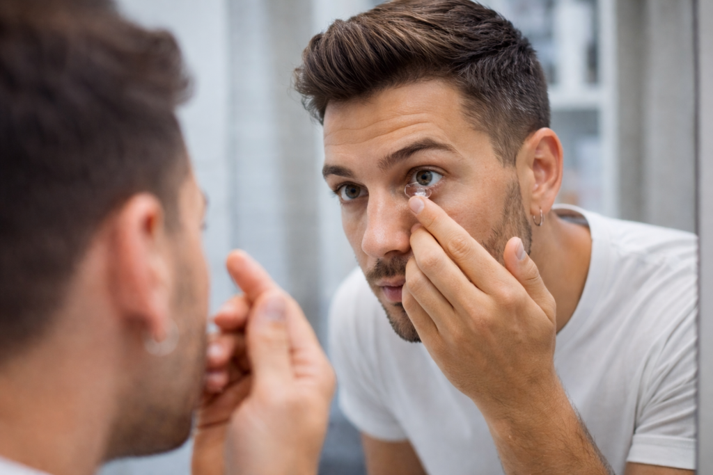 Junger Mann mit kurzen Haaren und T-Shirt setzt sich Kontaktlinse vor Spiegel ein